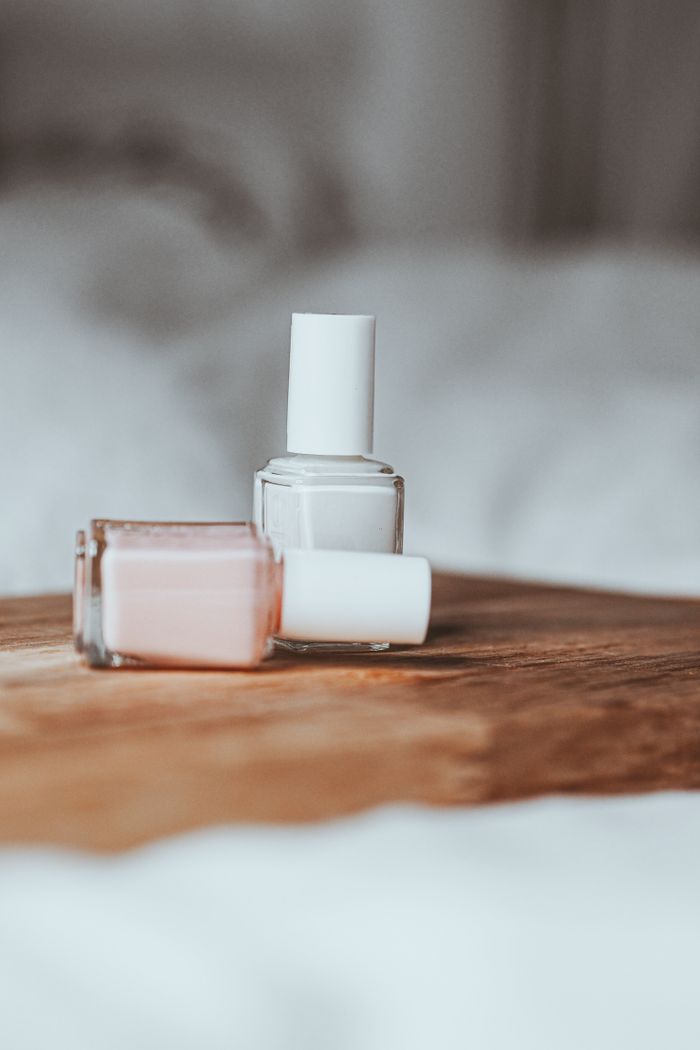Close-up of pink and white nail polish bottles on a wooden tray with a blurred background.