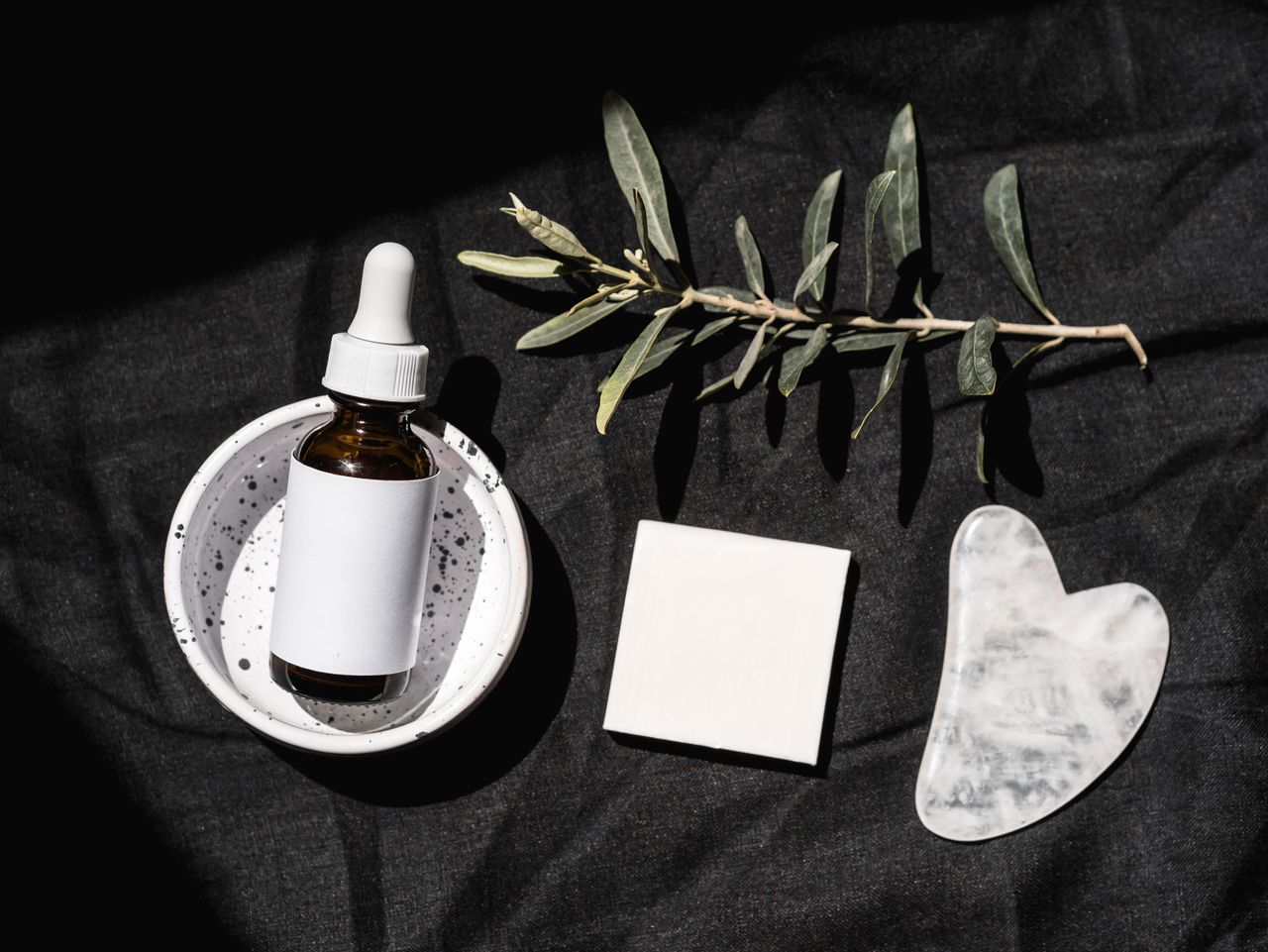 about-us-02 Elegant beauty product arrangement featuring a serum dropper bottle and gua sha on a black background.